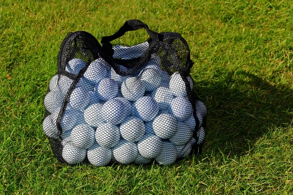 A mesh bag full of white golf balls on the grass