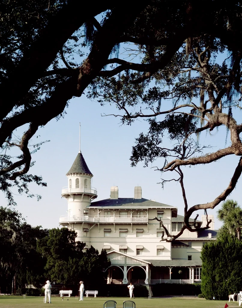 A white clubhouse with a turret, framed by oak branches