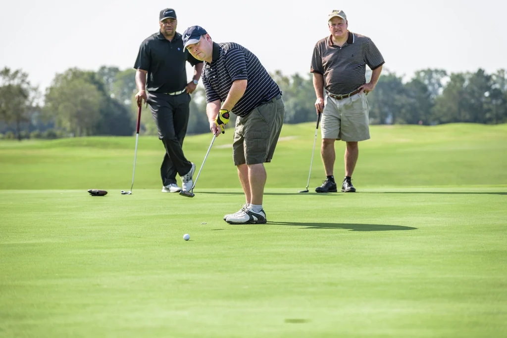 Three golfers on a green, one putting while the others watch