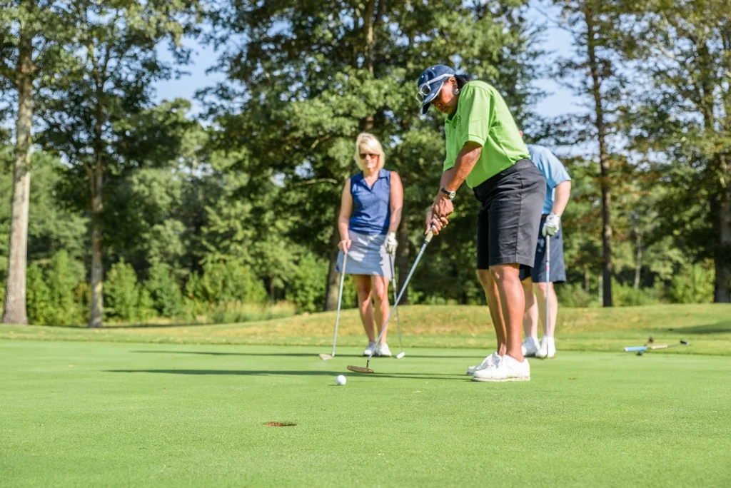 Three golfers on a practice green, one lining up a putt